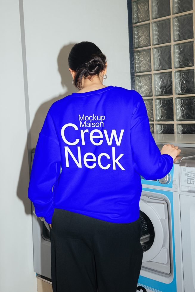 Woman in vibrant blue crew neck sweatshirt mockup, casual design, rear view, laundry room setting, realistic garment presentation for branding.