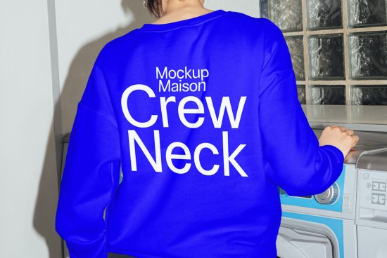 Rear view of person wearing blue crew neck sweater mockup with white text design in a laundry room setting, for graphic design and apparel mockups.