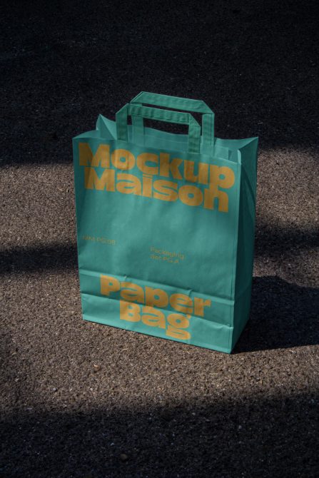 Green paper bag mockup with bold typography in sunlight on asphalt, perfect for designers looking to showcase branding or packaging designs.