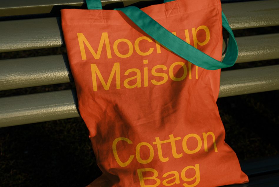 Red orange tote with yellow text, green handles displayed on metal bench