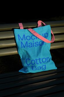 Turquoise cotton tote bag with blue text, coral handles on metal bench