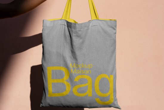 Tote bag mockup hanging against a pink wall with shadow, design presentation, canvas bag template, graphic design asset.