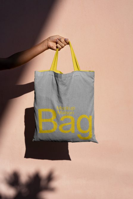 Person holding a tote bag mockup with yellow straps against a pink background for graphic design and branding display.