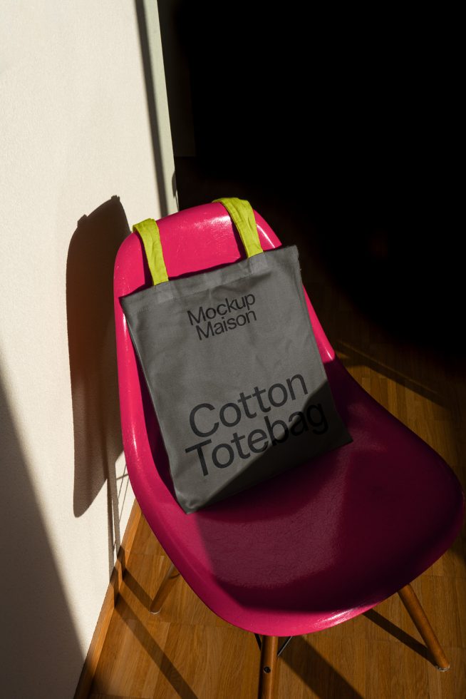 Stylish tote bag mockup on vibrant pink chair in sunlight for design presentation, ideal for showcasing patterns and branding designs.