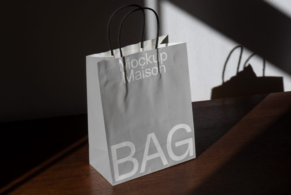 White paper shopping bag with black handles casting diagonal shadow on wall