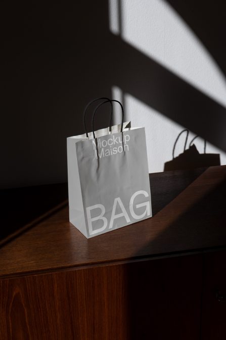 Minimalist white kraft paper bag with black handles lit by diagonal sunlight