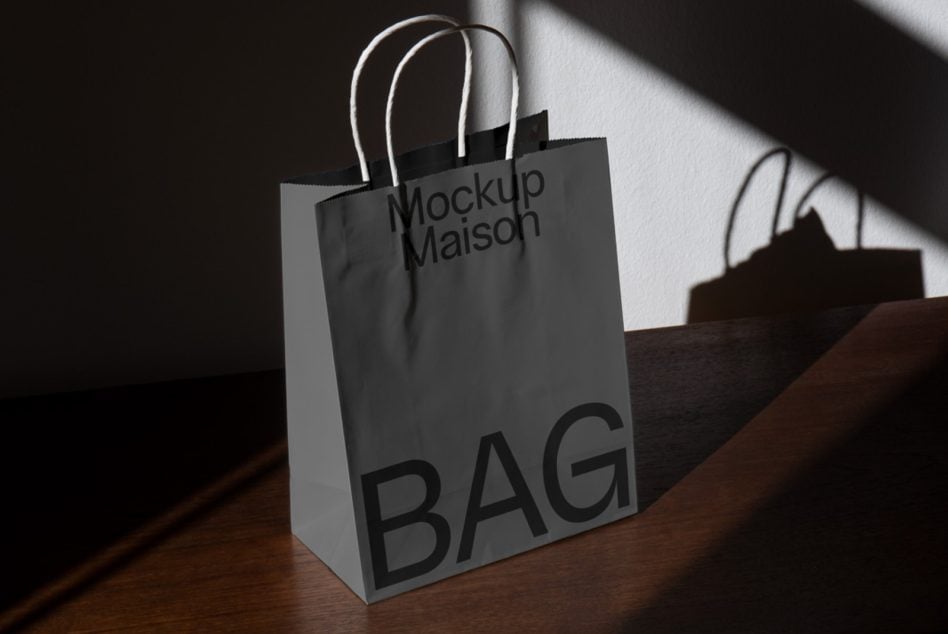 Gray paper shopping bag with rope handles creating dramatic shadows on surface