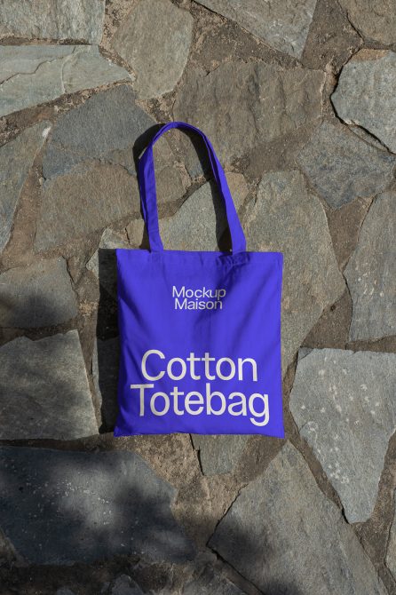 Blue tote bag mockup on a textured stone surface for graphic designers, perfect for showcasing branding and merchandising designs.