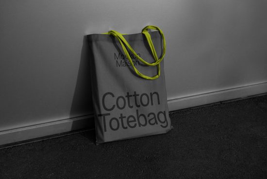 Gray cotton tote bag mockup with neon handles leaning against a wall, selective color, product design display.