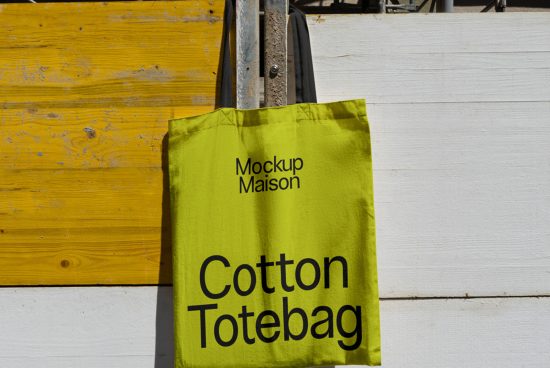 Bright green cotton tote bag mockup hanging on metal stand against yellow wooden background, clear design space.