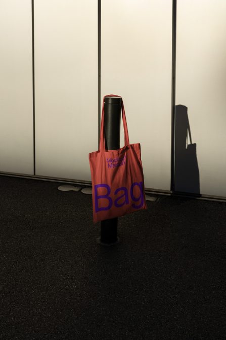 Reusable tote bag mockup hanging on street post with distinctive shadow, ideal for showcasing eco-friendly bag designs and modern typefaces.