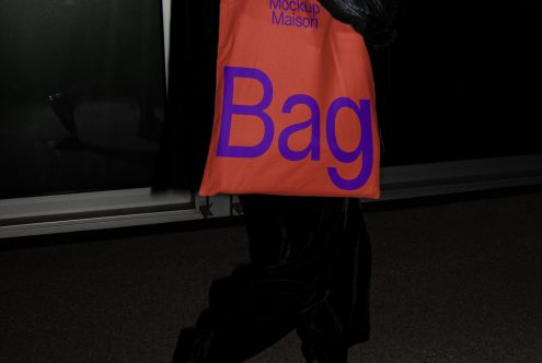 Person holding an orange tote bag mockup with purple text, ideal for design presentations and branding mockups in a street setting.