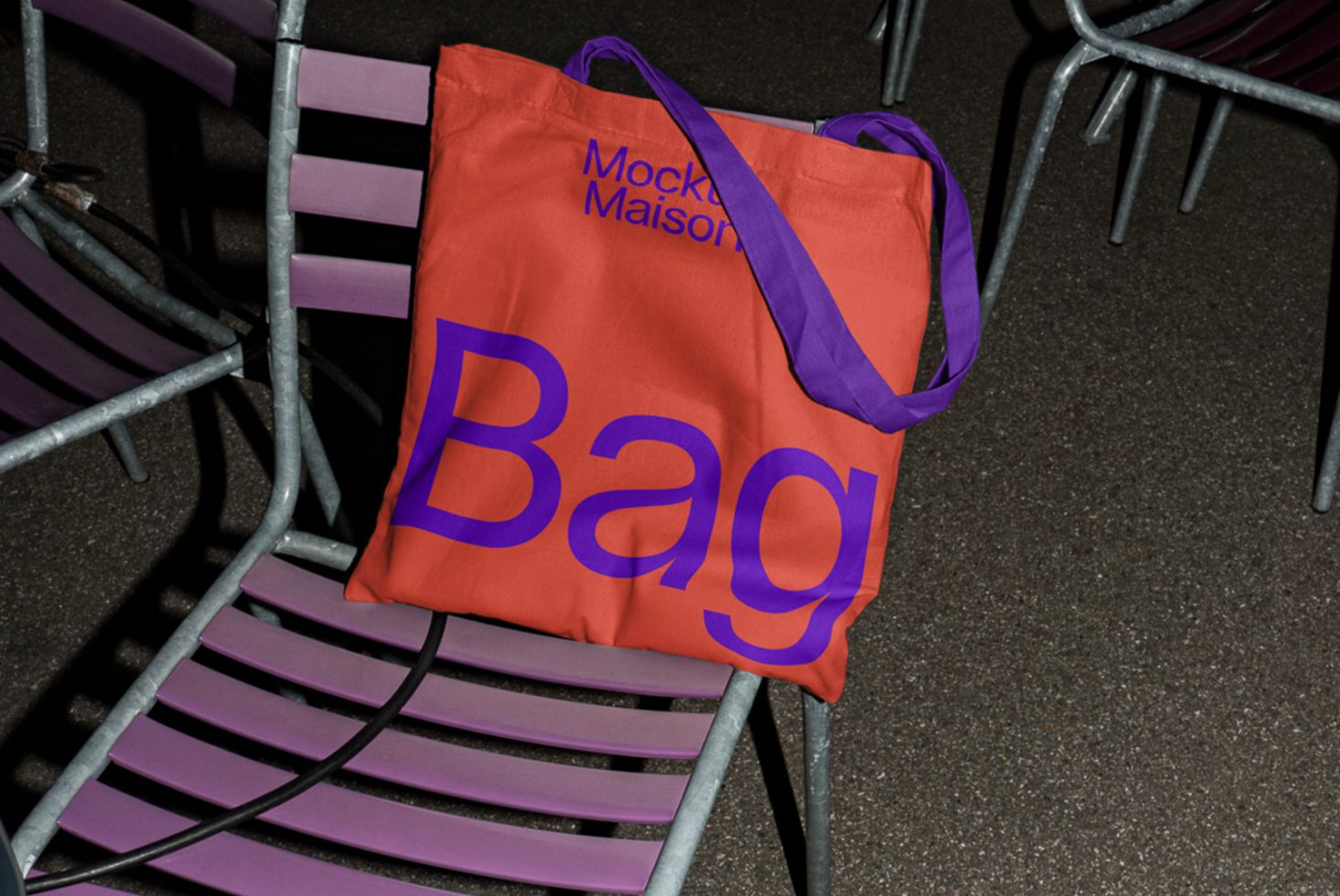 Orange tote bag with bold blue text on metal chairs, up-close texture, realistic mockup for branding, design presentation, urban style.