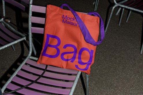 Orange tote bag with bold blue text on metal chairs, up-close texture, realistic mockup for branding, design presentation, urban style.