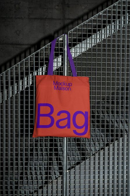 Tote bag mockup hanging on metal grid, concrete background, urban style design asset for product display and branding.