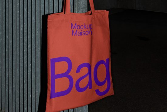 Red tote bag mockup leaning against a textured wall at night, showcasing bold typography design, ideal for graphic presentations.