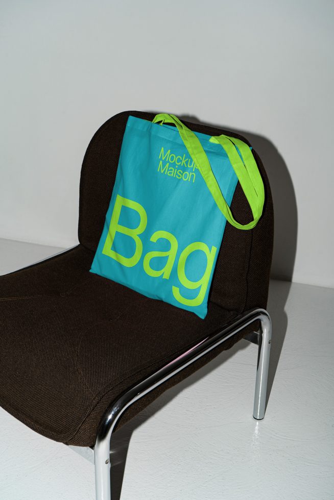 Tote bag mockup on modern chair, bright blue and lime design with text, ideal for showcasing fabric patterns and branding graphics.