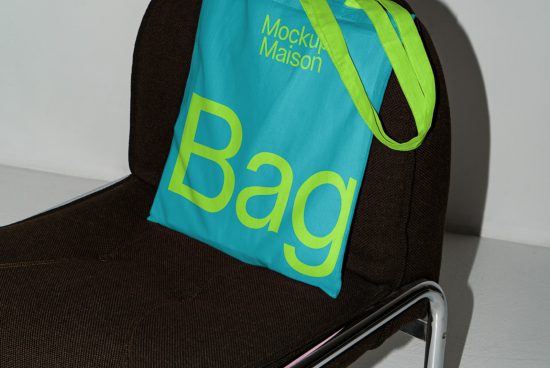 Bright cyan tote bag mockup with yellow text on a brown chair, showcasing bold graphic design and product presentation for designers.