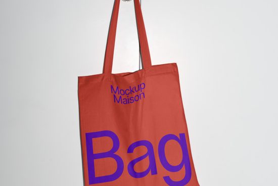 Red tote bag mockup with blue text hanging against a white background, perfect for showcasing designs and logos for designers.