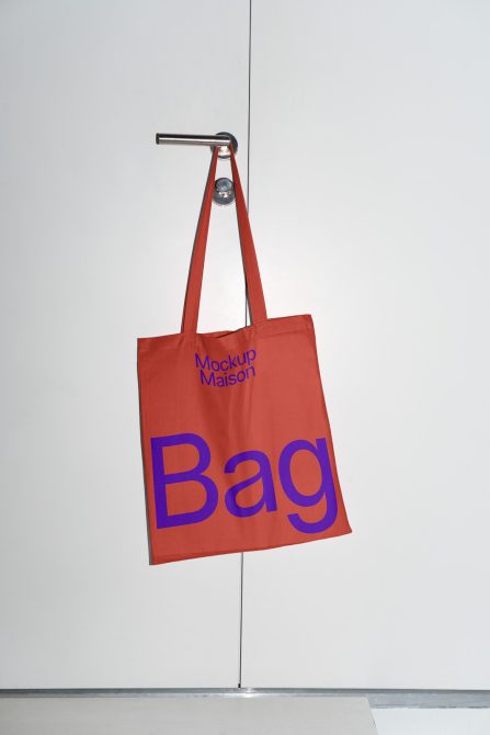 Red tote bag mockup hanging on metal peg against neutral background perfect for showcasing design work, tote bag mockups, realistic presentation.