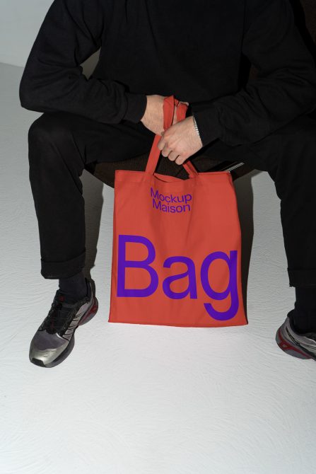 Person holding tote bag mockup with text, ideal for showcasing branding designs on digital marketplaces for creatives seeking graphics and templates.