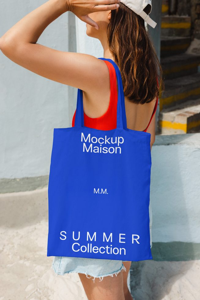 Woman in summer attire posing with a blue tote bag mockup, urban setting, ideal for design presentations, eCommerce, and branding assets.