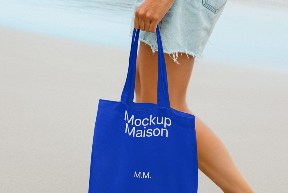 Royal blue tote held at beach with denim shorts, soft sand backdrop
