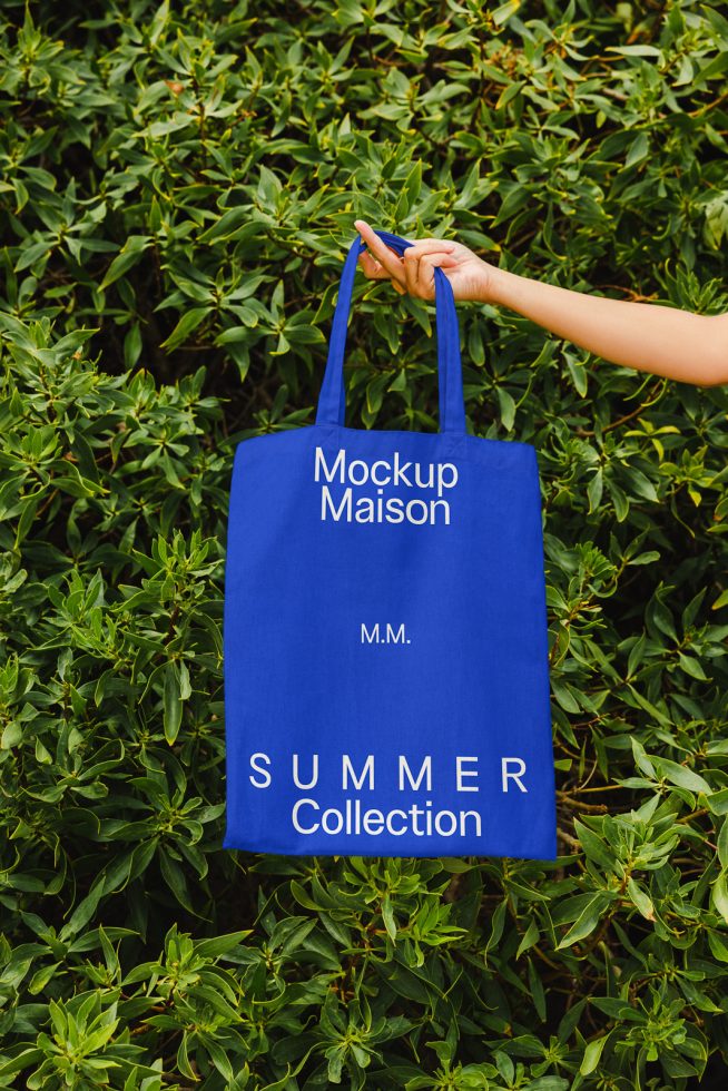 Blue tote bag mockup held against lush greenery for product design presentation and summer collection advertising, clear and vibrant display.