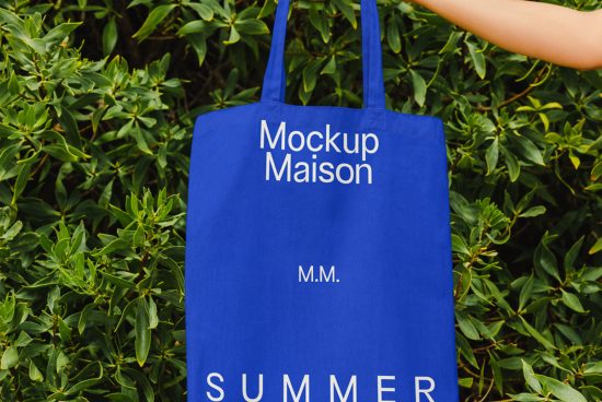 Blue tote bag mockup with white text 'Mockup Maison' held against green foliage background, ideal for eco-friendly design presentations.