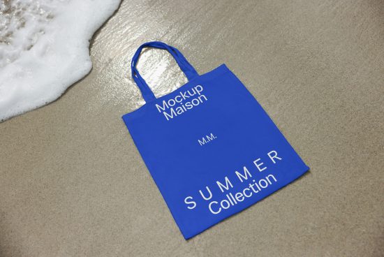 Blue tote bag mockup on sandy beach by water's edge, ideal for presenting summer collection designs, perfect for designers' product templates.