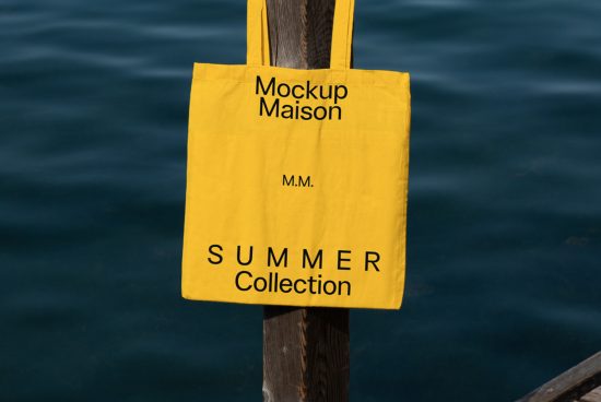 Yellow tote bag mockup hanging on wood post with sea background, showcasing bold typography for summer collection design asset.