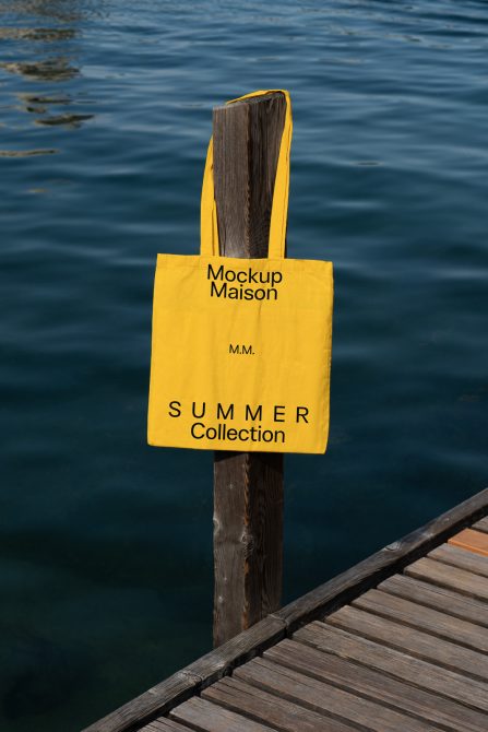 Yellow tote bag mockup hanging on wooden post by sea, clear branding space, summer collection theme, perfect for designers and graphic presentations.