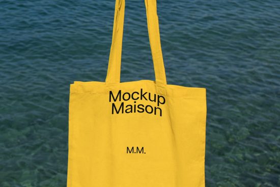 Yellow tote bag mockup with black typography design on it, floating over a blue water background, ideal for designers and branding.