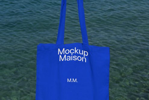 Blue tote bag mockup with white text design on water background, ideal for showcasing branding and merchandise designs.