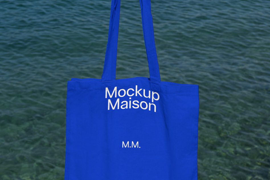 Blue tote bag mockup with white text design on water background, ideal for showcasing branding and merchandise designs.