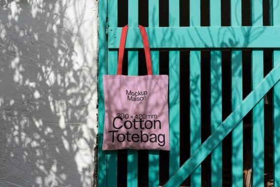 Cotton tote bag mockup hanging on turquoise fence with contrasting shadows. Realistic accessory template for design presentation.