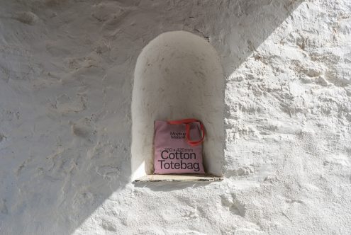 Mockup of a cotton tote bag with dimensions label, placed in a white textured alcove, casting shadow, ideal for realistic product display.