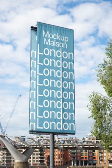 Tall teal billboard with repeated London text against blue sky, urban waterfront