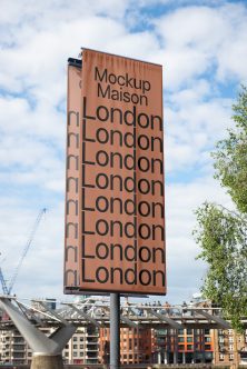 Tall terracotta billboard with repeated London text against blue sky, urban waterfront