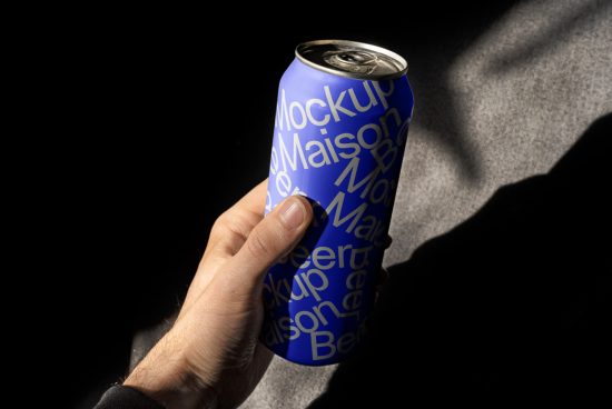 Hand holding blue beverage can mockup with typography design in sunlight and shadow, ideal for product mockups and branding design.