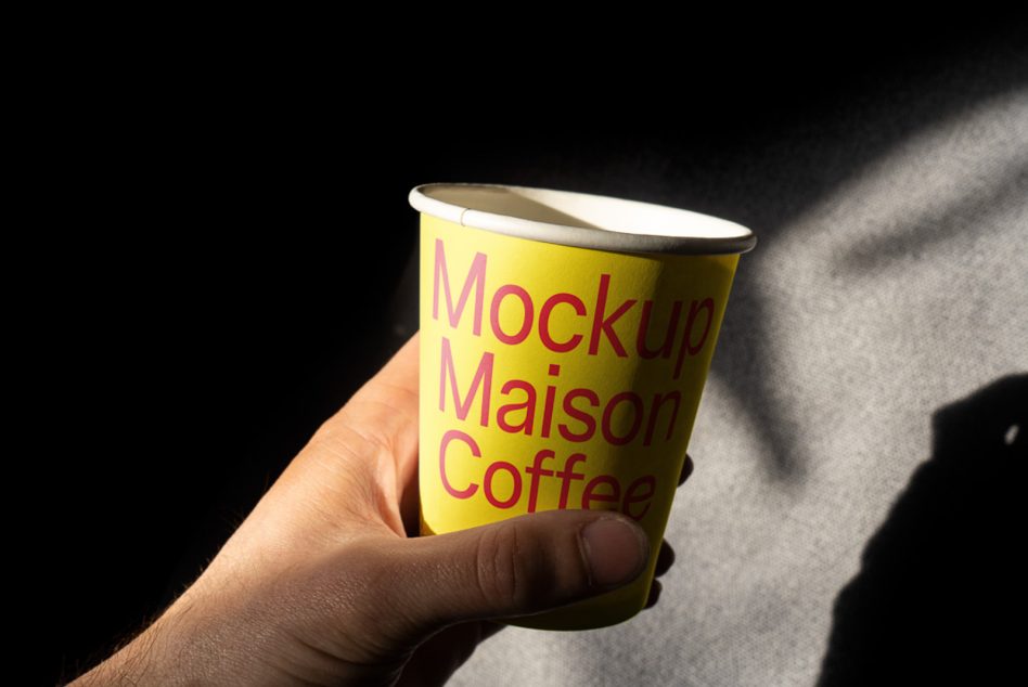 Yellow paper cup with red text held in hand against dark background