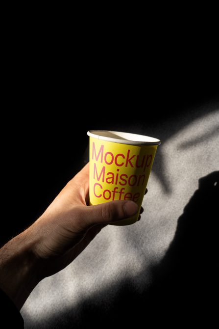 Hand holding yellow coffee cup with red text against bright sunlit fabric