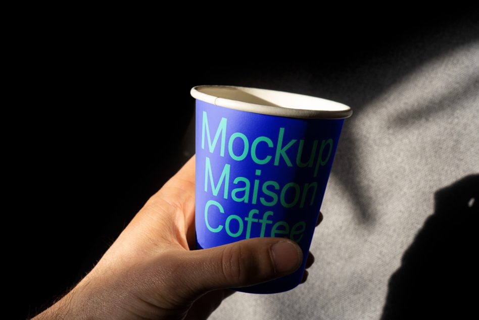 Hand gripping navy blue coffee cup with neon green text in natural lighting