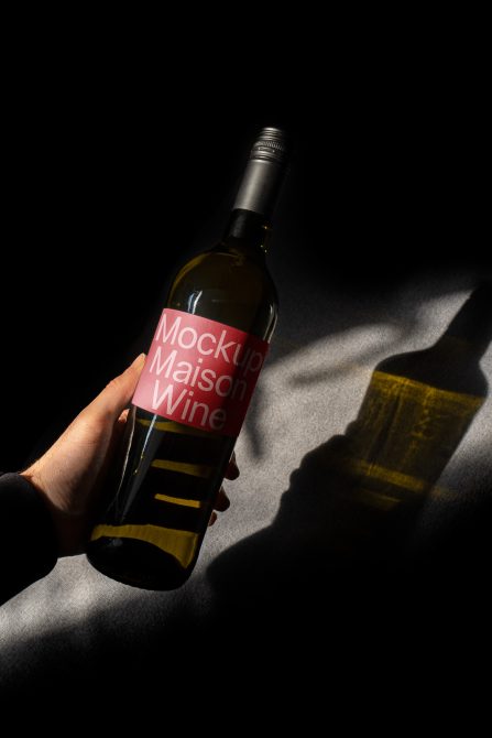 Hand holding wine bottle mockup with customizable label design, dramatic shadow overlay, ideal for presentations, in graphic design category.