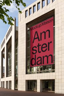 Red banner hanging on modern stone building window showing Amsterdam text