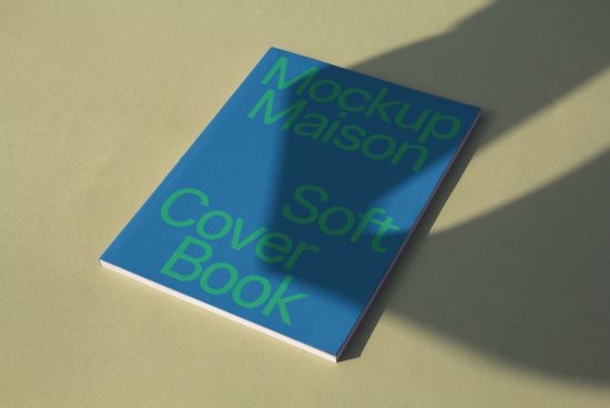 Mockup of blue soft cover book with green text on beige background, angled with shadows, realistic digital asset for designers.