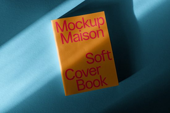 Yellow soft cover book mockup with pink title text, angled in dynamic shadowing on a blue background, ideal for graphic design presentations.