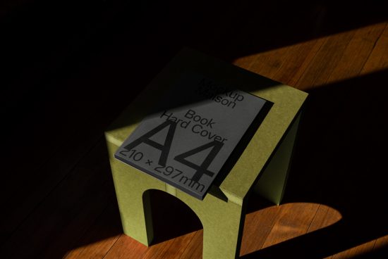 Realistic A4 hardcover book mockup on green stool with dramatic lighting, ideal for presentation and cover design.