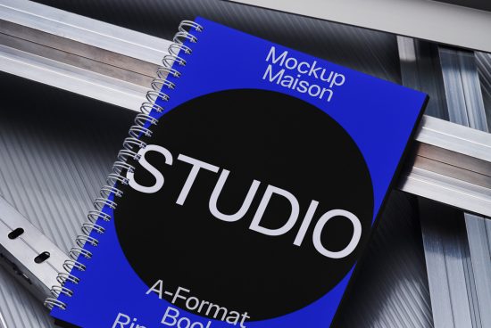 Realistic spiral notebook mockup with blue cover titled Mockup Maison lying on a metallic surface, graphic design asset for presentations.