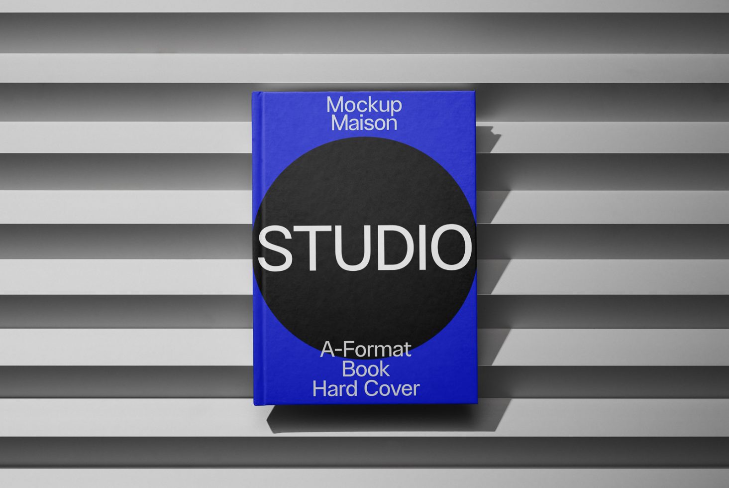 Blue hardcover book mockup with striking black circle on cover displayed on a striped gray background, ideal for presenting design work.